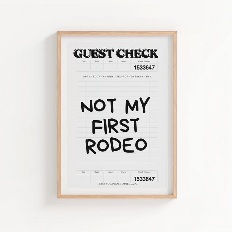 May include: Framed print featuring a mock guest check design. The top reads "GUEST CHECK" and includes a check number. The phrase "NOT MY FIRST RODEO" is prominently displayed in bold, black letters. The print is in a light wood frame.