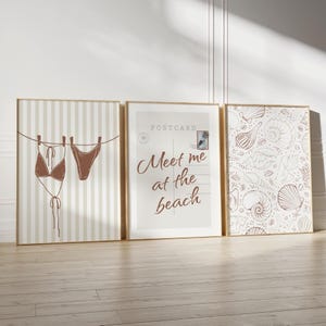 May include: Three framed beach-themed art prints. The left print features a brown bikini hanging on a clothesline against a striped background. The center print says "Meet me at the beach". The right print has a seashell pattern.