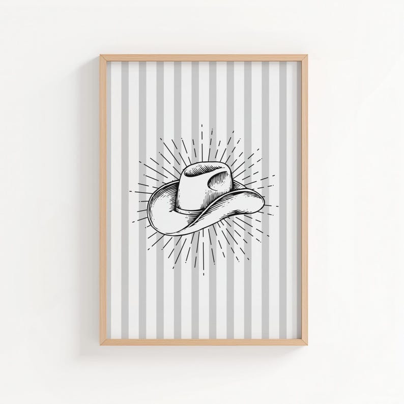 May include: A framed print featuring a black and white illustration of a cowboy hat. The hat is centered on a background of vertical gray and white stripes. The hat is surrounded by a sunburst design.