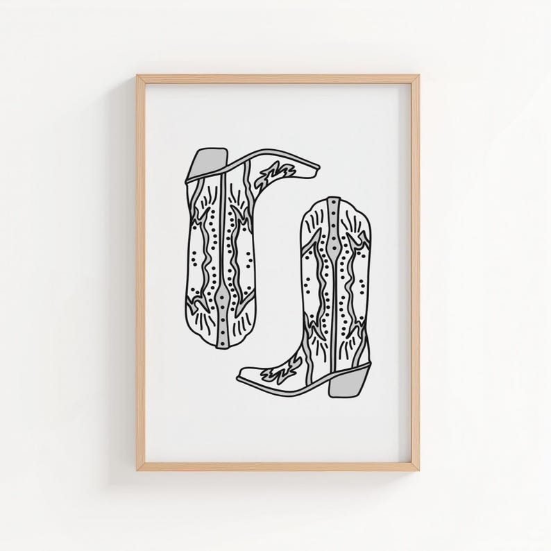 May include: A framed print featuring a pair of cowboy boots. The boots are depicted in a black and white line drawing style, with intricate decorative patterns. The boots are set against a white background, and the frame is a light wood color.