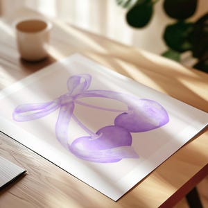 May include: A watercolor illustration printed on paper featuring two heart-shaped cherries in a light purple hue, connected by stems and tied together with a delicate, flowing purple ribbon that loops around the fruit in a soft, artistic style.