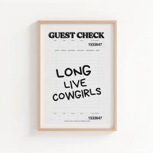 May include: A framed print featuring a stylized "Guest Check" design. Bold black text at the top reads "GUEST CHECK" and "1533647". Below, the words "LONG LIVE COWGIRLS" are written in a playful font. The print is in a light wood frame.