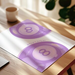 May include: A white rectangular print featuring two purple illustrations of eight balls, each with a central circle containing the number eight. The text "Lucky girl, lucky me" is printed in a purple script font between the two eight ball graphics.