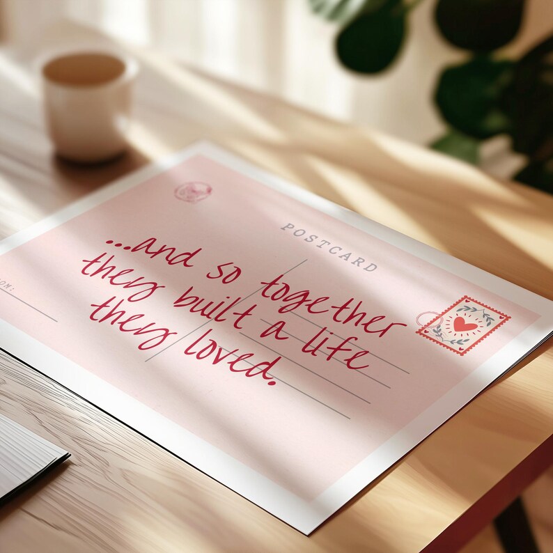 Puede incluir: Una postal rectangular con fondo rosa claro que presenta el texto manuscrito en rojo oscuro, "...and so together they built a life they loved." La postal incluye una peque&ntilde;a ilustraci&oacute;n de un sello de coraz&oacute;n rojo y la palabra "POSTCARD" en la esquina.