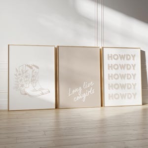 Könnte beinhalten: Ein Set aus drei gerahmten Wandbildern. Das linke Bild zeigt eine Strichzeichnung von Cowboystiefeln mit Blumen. Das mittlere Bild hat einen beigen Hintergrund mit dem weißen Text Long live cowgirls. Das rechte Bild wiederholt das Wort HOWDY fünfmal.