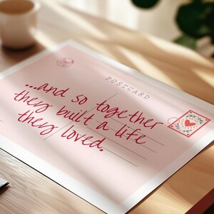 Puede incluir: Una postal rectangular con fondo rosa claro que presenta el texto en cursiva de color rojo oscuro: "...and so together they built a life they loved." La tarjeta incluye la palabra "POSTCARD" en la parte superior derecha y un sello decorativo con un coraz&oacute;n rojo.