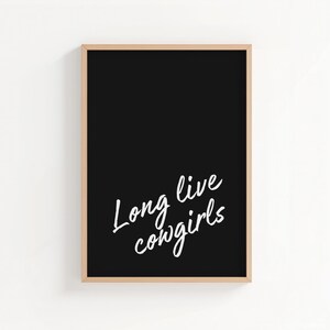 May include: A framed art print with a black background and the white text "Long live cowgirls." The frame is a light brown color. The artwork is a simple, yet bold statement piece.