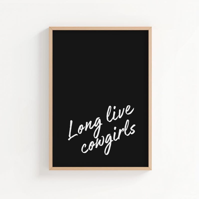 May include: A framed art print with a black background and the white text "Long live cowgirls." The frame is a light brown color. The artwork is a simple, yet bold statement piece.