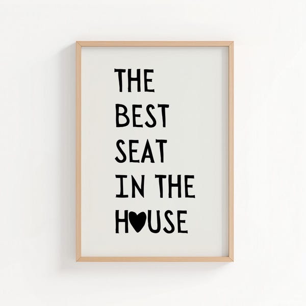 Puede incluir: Un cuadro decorativo con el texto negro THE BEST SEAT IN THE HOUSE sobre un fondo blanco. La letra O en la palabra HOUSE está reemplazada por un corazón negro sólido. La lámina está dentro de un marco de madera de color claro.