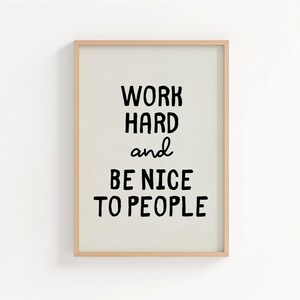 Può includere: Una stampa artistica rettangolare da parete in una cornice di legno chiaro con il testo nero WORK HARD and BE NICE TO PEOPLE centrato su uno sfondo color crema. La tipografia usa un mix di lettere in grassetto e un corsivo per la parola and.