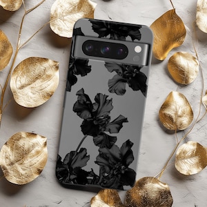 Può includere: Una custodia per telefono in bianco e nero con un design floreale. La custodia ha un ritaglio per l'obiettivo della fotocamera e uno sfondo nero con fiori bianchi.