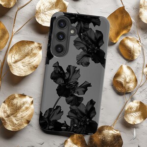 Peut inclure: Une coque de téléphone grise avec un motif floral noir. La coque a une découpe pour l'objectif de l'appareil photo avec trois lentilles.