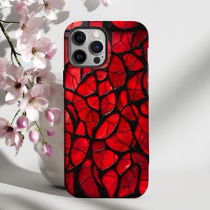 Op de afbeelding: Een rode en zwarte telefoonhoes met een geometrisch patroon. De hoes is gemaakt van hard plastic en heeft een verhoogde camerabult.