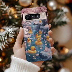 Puede incluir: Una funda de teléfono con un diseño floral rosa y blanco y una imagen de patos de goma amarillos flotando en un arroyo azul con flores rosas.