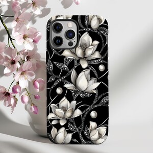 Puede incluir: Carcasa de teléfono negra con un diseño floral blanco. Las flores son magnolias con detalles de perlas. La carcasa tiene un fondo negro con enredaderas plateadas.