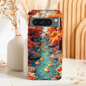 Puede incluir: Una funda para teléfono con una escena de bosque de otoño colorido y una línea de patos de goma amarillos flotando por un arroyo. La funda tiene un recorte de cámara negro y un recorte de flash blanco.