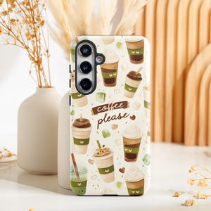 May include: A phone case with a cream background featuring a pattern of coffee drinks, hearts, and green accents. The phrase "coffee please" is written on a brown banner. The case has a camera cutout.