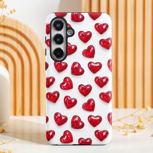 May include: A white phone case with a pattern of red hearts. The case has a cutout for the camera lens.