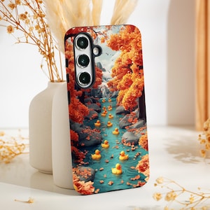 Puede incluir: Una funda para teléfono con una escena de otoño colorida que presenta una corriente de patos de goma amarillos. La funda tiene un recorte de cámara negro y una superficie texturizada.