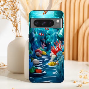 May include: A phone case featuring a vibrant underwater scene with clownfish, coral, and seashells. The design showcases a blue and turquoise color palette, creating a 3D effect. The case is designed to fit a smartphone.