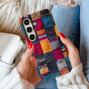 May include: A multi-coloured phone case with a patchwork design. The case features squares of fabric in shades of red, blue, yellow, and black. The phone case is held by a person with red nail polish.