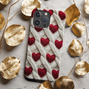 May include: White phone case with a knitted pattern and red hearts. The case has a camera lens cutout and a white background.