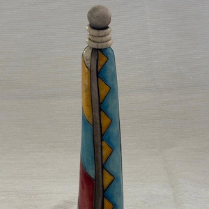 May include: A tall, decorative bottle with a rounded top and a geometric design. The bottle features a light blue body with yellow and red accents. The top is a light gray color.