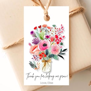 May include: A white gift tag with a colorful floral bouquet illustration. The bouquet is in a mason jar and has pink, red, orange, yellow, purple, and green flowers. The text on the tag reads 'Thank you for helping me grow! Love, Elise'.