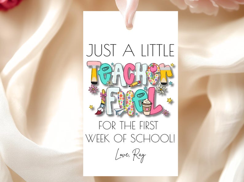 May include: A white gift tag with the text "JUST A LITTLE TEACHER FUEL FOR THE FIRST WEEK OF SCHOOL! Love, Ray." The text is in various colors and includes illustrations of school supplies and a coffee cup.