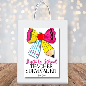 May include: White gift bag featuring a colourful graphic of a bow made from a pencil, ribbon, and apple. The text on the bag reads "Back to School TEACHER SURVIVAL KIT" in pink and black. The bag has white handles and is on a wooden surface.