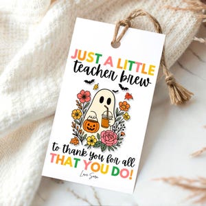 Puede incluir: Una etiqueta de regalo blanca con una ilustraci&oacute;n de un fantasma sosteniendo una calabaza y una bebida. La etiqueta dice "JUST A LITTLE teacher brew to thank you for all THAT YOU DO!" en texto colorido, con una cuerda de yute adjunta.