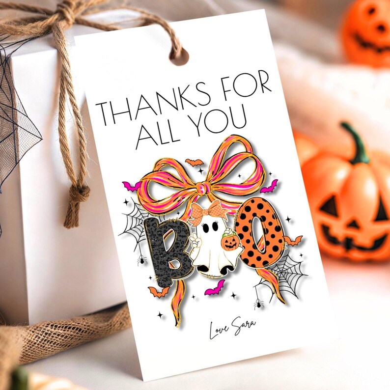 May include: A white gift tag with the text "THANKS FOR ALL YOU" and a Halloween-themed design. The design includes a bow, the word "BOO", a ghost, bats, and spiderwebs. The tag is tied to a white gift box with twine.