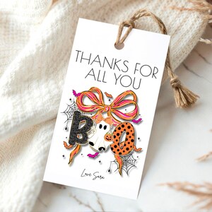 May include: A white Halloween gift tag with the words "THANKS FOR ALL YOU" at the top. The word "BOO" is in the center, with a ghost, a pumpkin, and a bow. The tag is tied with a brown string and has the words "Love Sara" at the bottom.