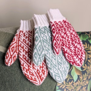 May include: Three crocheted mittens in red, green, and white with a geometric pattern.