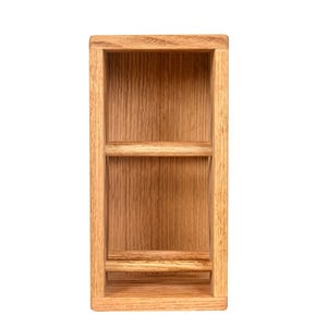 May include: A rectangular wooden shelf with a recessed interior and two horizontal shelves. The wood has a natural, light brown color and visible grain. The shelf is designed for storage or display.