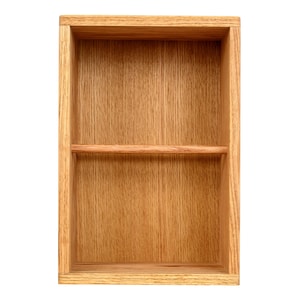 May include: A rectangular wooden shelf with a natural wood grain finish. The shelf has a single horizontal divider, creating two compartments. The wood has a warm, light brown color.
