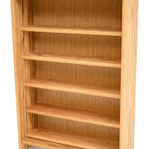 May include: A light-colored wooden shelf unit with five shelves. The shelves are evenly spaced and the unit has a simple, functional design. The wood grain is visible, giving it a natural look. The unit is suitable for displaying items.