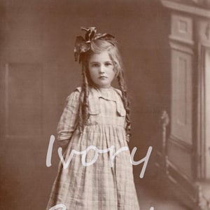May include: A young girl in a plaid dress with a large bow in her hair. She is wearing white socks and black shoes. The photo is in black and white.