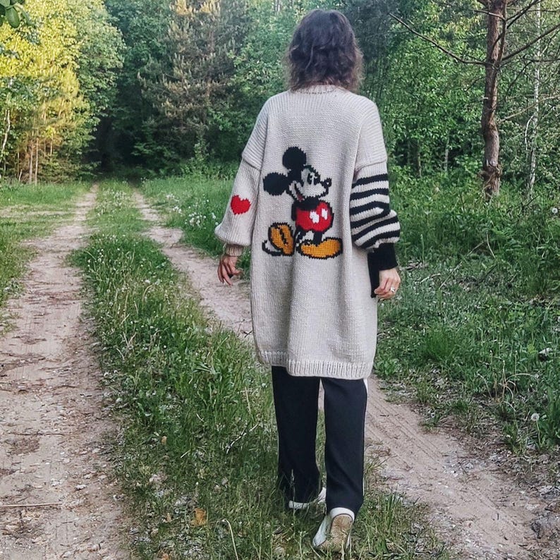 May include: A white knitted cardigan with a Mickey Mouse graphic on the back. The cardigan has red hearts on the sleeves and black and white stripes on the other sleeve.