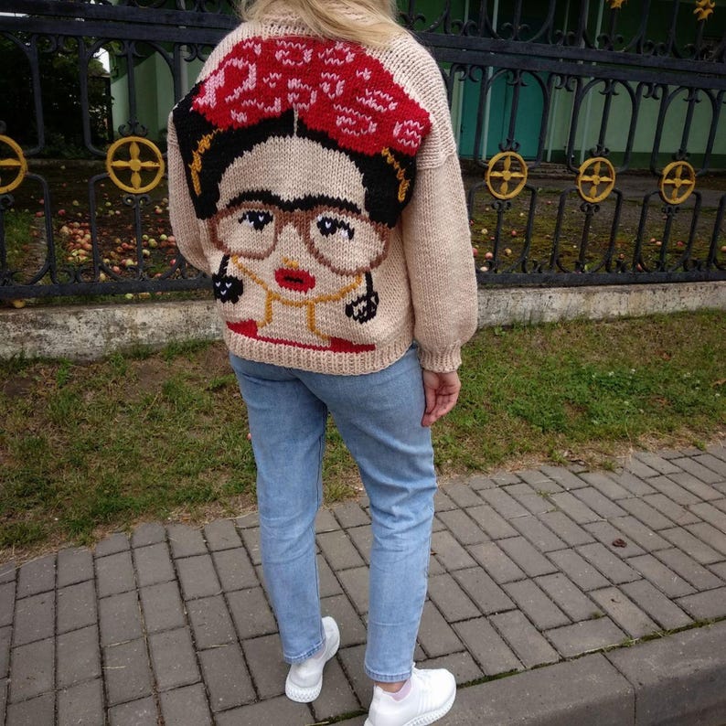 Pode incluir: Um su&eacute;ter de tric&ocirc; bege com uma imagem bordada colorida de Frida Kahlo nas costas. O su&eacute;ter tem um caimento solto e mangas compridas.