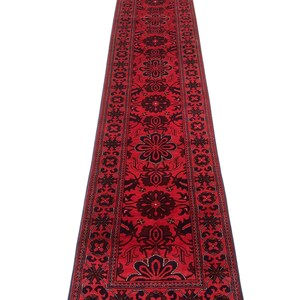 May include: A red runner rug with a traditional Persian design featuring intricate floral patterns in black and navy blue. The rug has a fringe border.