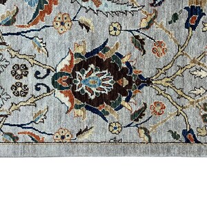 Puede incluir: Primer plano de una secci&oacute;n de una alfombra gris con un intrincado dise&ntilde;o floral. El dise&ntilde;o presenta elementos florales marrones, azules, naranjas y verdes sobre un fondo gris. La alfombra tiene una apariencia detallada y texturizada.