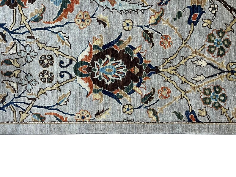 Puede incluir: Primer plano de una secci&oacute;n de una alfombra gris con un intrincado dise&ntilde;o floral. El dise&ntilde;o presenta elementos florales marrones, azules, naranjas y verdes sobre un fondo gris. La alfombra tiene una apariencia detallada y texturizada.