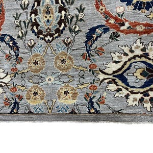 Puede incluir: Primer plano de una alfombra gris con un intrincado dise&ntilde;o floral. El dise&ntilde;o presenta acentos marrones, azules y rojos sobre un fondo gris claro. El borde de la alfombra es gris oscuro y el estilo general es tradicional.