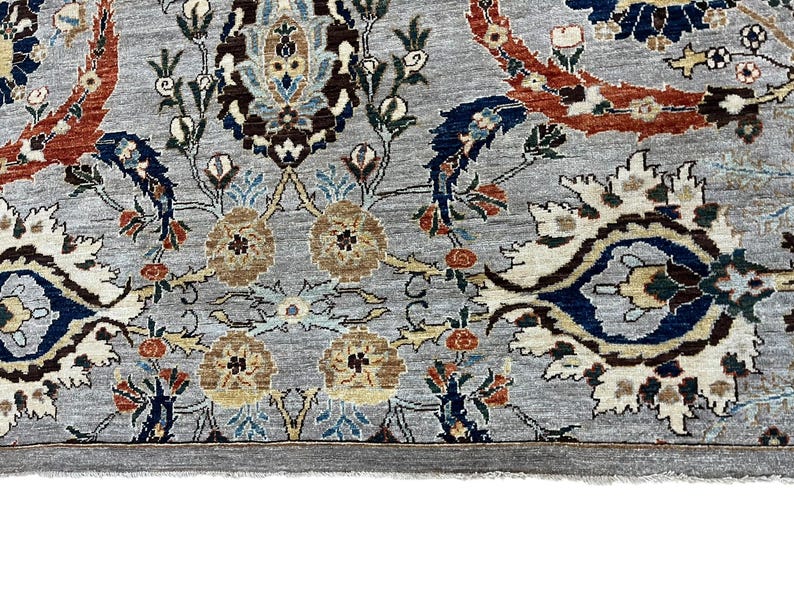 Puede incluir: Primer plano de una alfombra gris con un intrincado dise&ntilde;o floral. El dise&ntilde;o presenta acentos marrones, azules y rojos sobre un fondo gris claro. El borde de la alfombra es gris oscuro y el estilo general es tradicional.