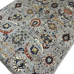 Puede incluir: Una alfombra gris con un intrincado dise&ntilde;o floral. La alfombra presenta un dise&ntilde;o central de flores y hojas estilizadas en tonos de azul, rojo, marr&oacute;n y crema. El borde de la alfombra es de un gris m&aacute;s oscuro.