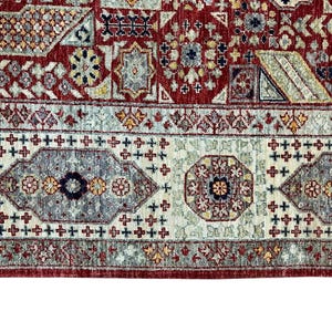 Puede incluir: Primer plano de una secci&oacute;n de una alfombra estampada en rojo, beige y gris. La alfombra presenta un dise&ntilde;o complejo con formas geom&eacute;tricas, motivos florales y un borde con patrones de cruces y oct&aacute;gonos repetidos. La paleta de colores incluye rojo, beige, gris y toques de amarillo.