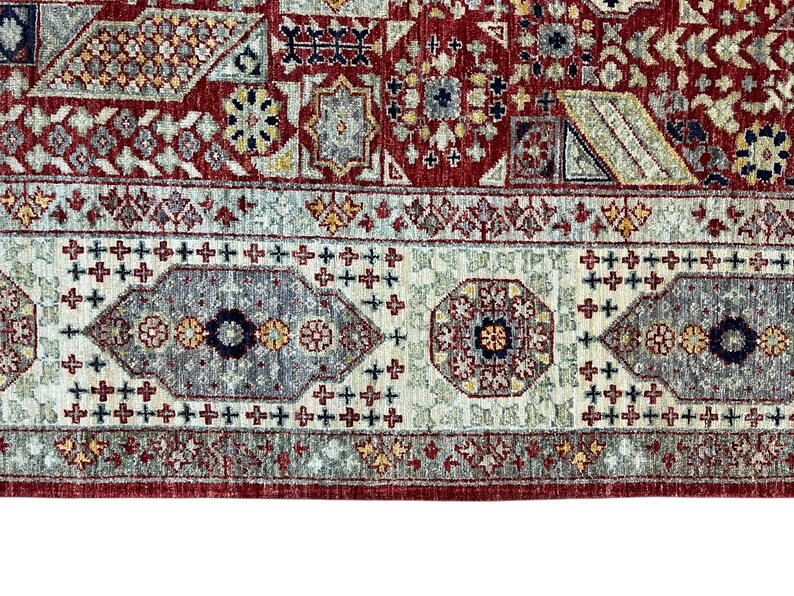 Puede incluir: Primer plano de una secci&oacute;n de una alfombra estampada en rojo, beige y gris. La alfombra presenta un dise&ntilde;o complejo con formas geom&eacute;tricas, motivos florales y un borde con patrones de cruces y oct&aacute;gonos repetidos. La paleta de colores incluye rojo, beige, gris y toques de amarillo.