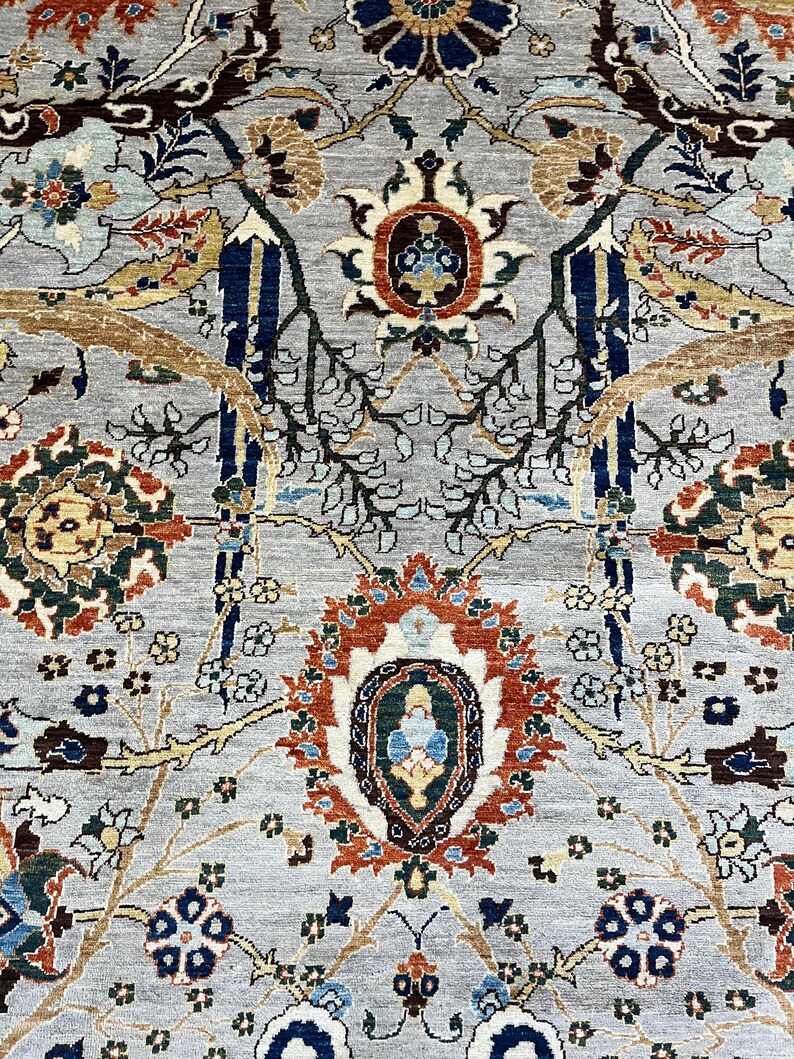 Puede incluir: Primer plano de una alfombra gris con un intrincado dise&ntilde;o floral. El dise&ntilde;o presenta un medall&oacute;n central en tonos naranja, azul y marr&oacute;n, rodeado de detallados motivos florales y de vid en varios colores. La alfombra tiene un aspecto suave y texturizado.