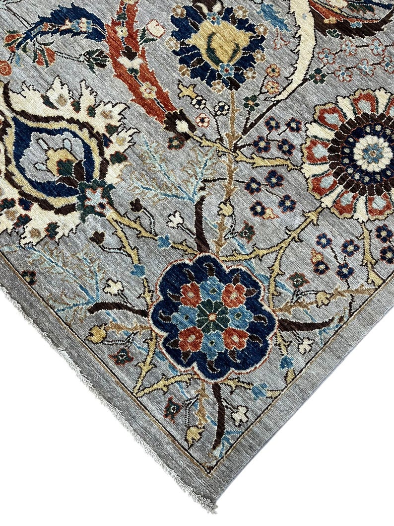 Puede incluir: Primer plano de una alfombra gris con un intrincado dise&ntilde;o floral. El dise&ntilde;o presenta flores y hojas azules, rojas y crema sobre un fondo gris. La alfombra tiene un borde detallado y un borde con flecos.